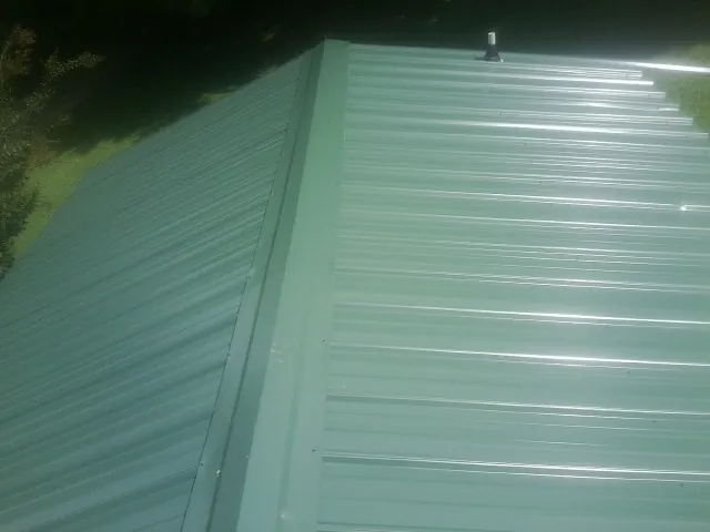 New green metal panels meeting at the ridge of a roof — Flat Roof Repair work by our crew in Batavia